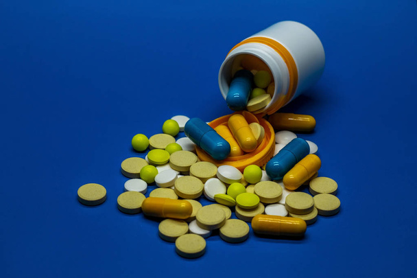 Diferentes pílulas farmacêuticas coloridas e cápsulas espalhadas de um frasco. O conceito de saúde e medicina. Fundo azul
. - Foto, Imagem