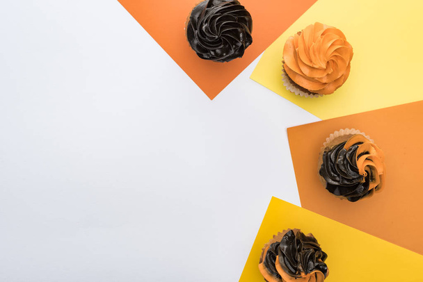 Draufsicht auf köstliche Halloween-Cupcakes auf gelbem, orangefarbenem und weißem Hintergrund mit Kopierfläche - Foto, Bild