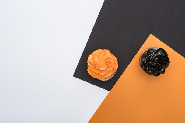 top view of delicious Halloween cupcakes on black, orange and white background with copy space - Fotoğraf, Görsel