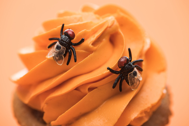 close up view of spooky Halloween cupcake with flies on cream isolated on orange - Fotó, kép