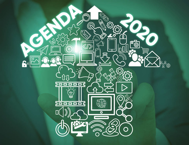 Writing note showing Agenda 2020. Business photo showcasing list of activities in order which they are to be taken up Male wear formal work suit presenting presentation smart device. - Photo, Image