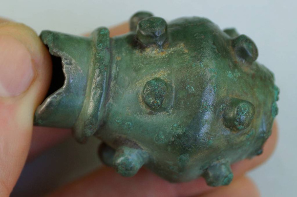 vingers houden een oude groene bronzen Mace op een grijze achtergrond - Foto, afbeelding