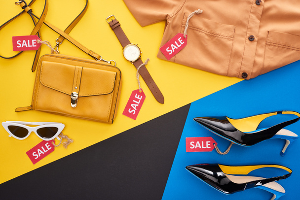 bovenaanzicht van kleding, schoenen en accessoires met verkooplabels op blauwe, gele en zwarte achtergrond - Foto, afbeelding