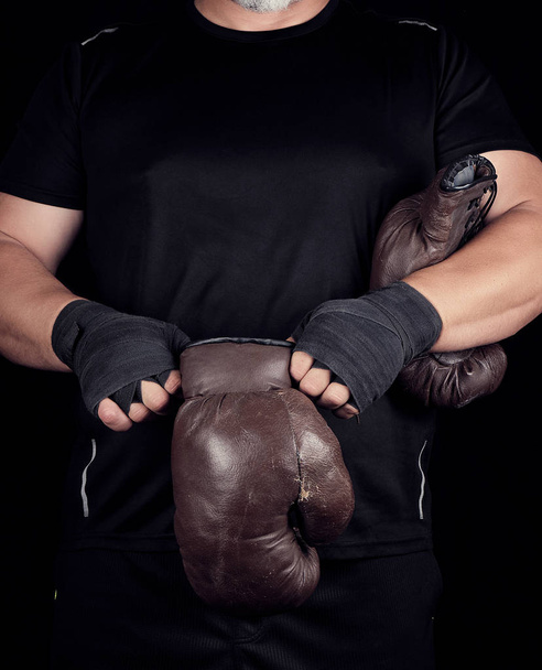 adult muscular man in black clothes puts on leather brown boxing - Photo, Image