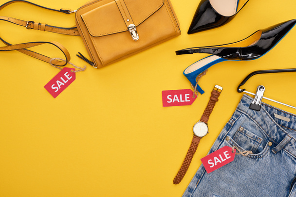 bovenaanzicht van modieuze kleding en accessoires met verkooplabels op gele achtergrond - Foto, afbeelding