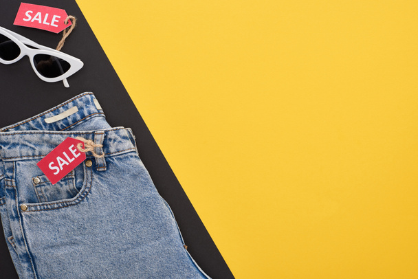 top view of jeans and glasses with sale labels on yellow and black background - Fotografie, Obrázek