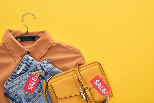 top view of bag, shirt and jeans with sale labels isolated on yellow - Photo, Image