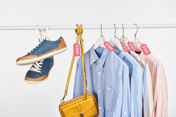 zapatillas, bolsos y camisas elegantes colgando con etiquetas de venta aisladas en blanco
 - Foto, imagen