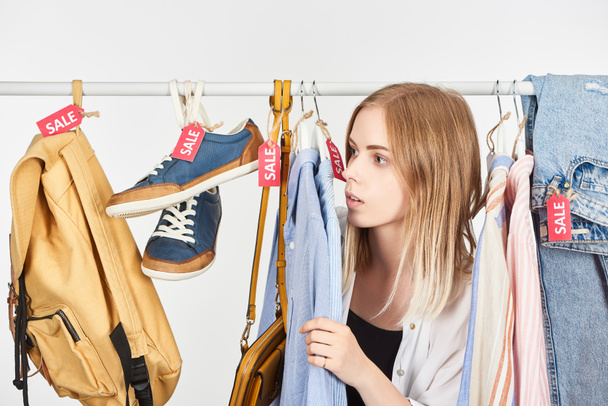 blond meisje in modieuze kleding opknoping met verkoop labels geïsoleerd op wit - Foto, afbeelding