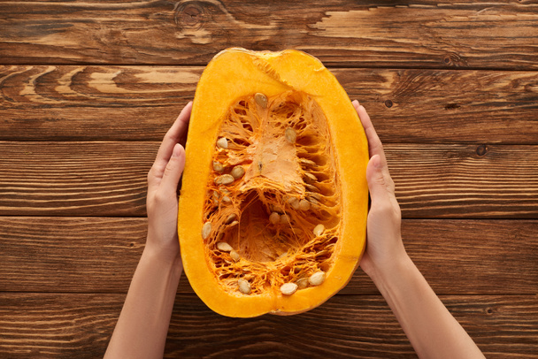 cropped view of woman holding half of pumpkin on brown wooden surface - Photo, Image