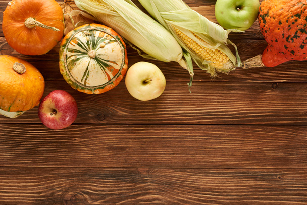 top view of raw sweet corn, pumpkins and apples on brown wooden surface - Fotó, kép