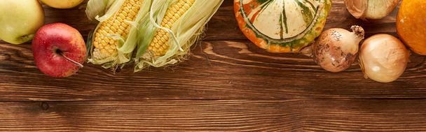 panoramic shot of raw sweet corn, pumpkins, onions and apples on brown wooden surface - Fotoğraf, Görsel