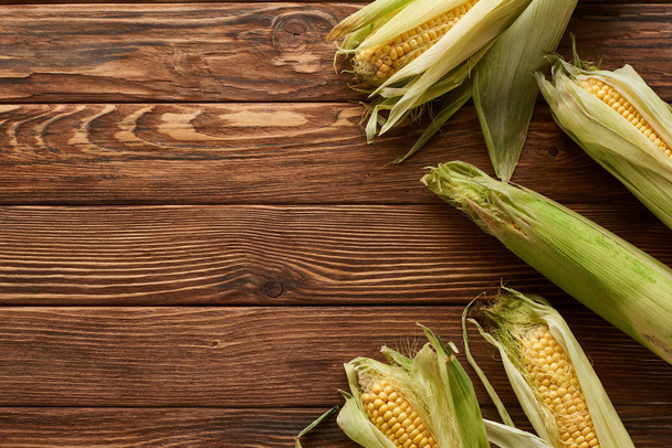 top view of raw sweet corn on brown wooden surface - Fotó, kép