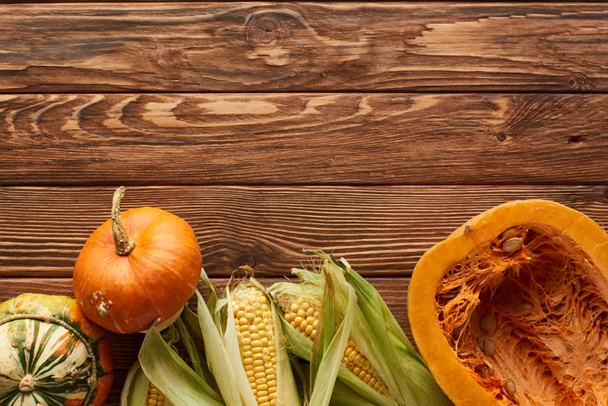 top view of raw sweet corn, whole pumpkin and half on brown wooden surface - Fotoğraf, Görsel