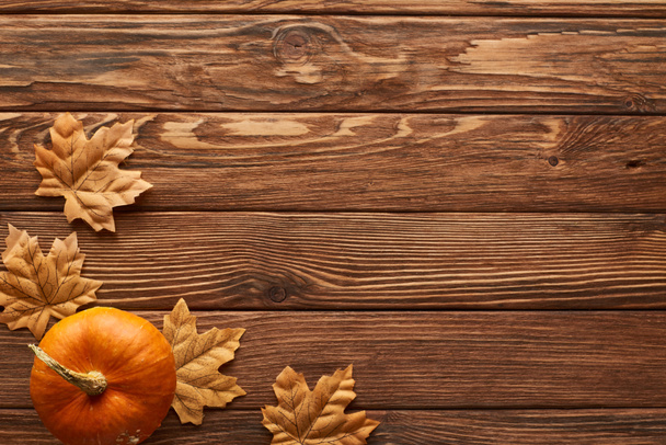 pohled na malou dýni na hnědém dřevěném povrchu se sušenými podzimními listy - Fotografie, Obrázek
