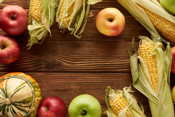 top view of uncooked sweet corn, ripe apples and pumpkin on wooden surface with copy space - Fotografie, Obrázek