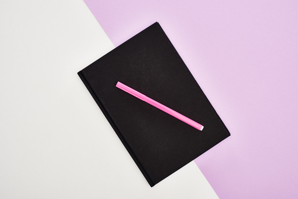 tendido plano con cuaderno negro con pluma de fieltro rosa sobre fondo violeta y blanco
 - Foto, imagen