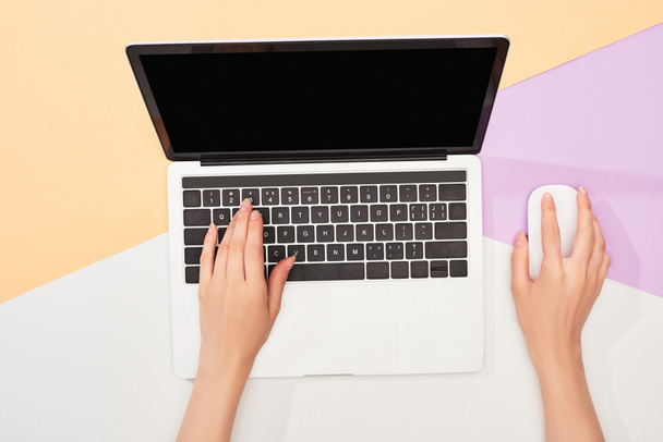 cropped view of woman using laptop and computer mouse on beige, violet and white background - Foto, afbeelding