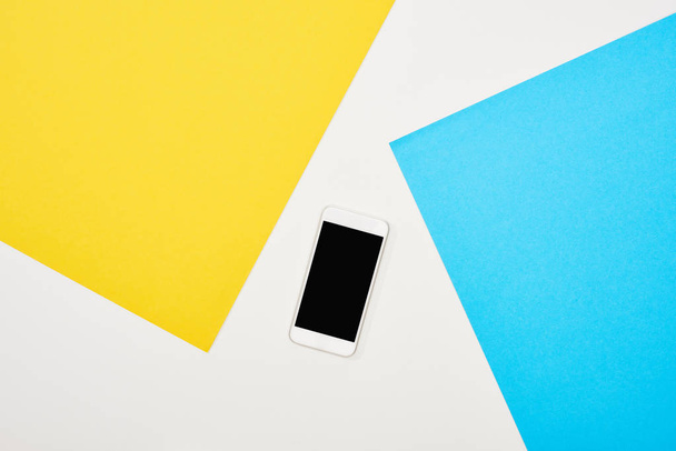 top view of smartphone with blank screen on yellow, blue and white background - Foto, afbeelding