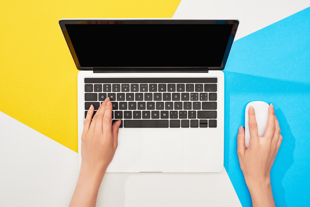 przycięte widok kobiety za pomocą laptopa z pustym ekranem i myszy komputerowej na żółtym, niebieskim i białym tle - Zdjęcie, obraz