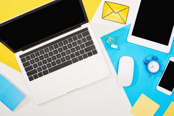 top view of digital devices with office supplies and mail icon on yellow, blue and white background - Foto, Bild