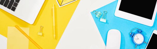 top view of laptop, smartphone, digital tablet with blank screen and computer mouse with office supplies on yellow, blue and white background - Photo, Image