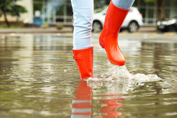 Woman with red rubber boots in puddle, closeup. Rainy weather - Foto, Bild