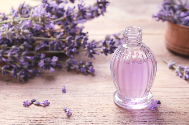 Lasipullo luonnonkosmetiikkaöljyä ja laventelin kukkia puupöydällä, tilaa tekstille
 - Valokuva, kuva