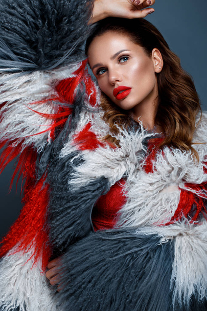 Όμορφη γυναίκα με κλασικό εορταστικό make-up, κόκκινα χείλη, μπούκλες σε ένα πολύχρωμο llama παλτό. Πρόσωπο ομορφιάς. - Φωτογραφία, εικόνα