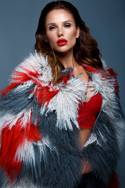 Beautiful woman with classic holiday make-up, red lips, curls in a multi-colored llama coat. Beauty face. - Фото, изображение