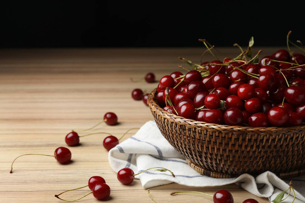 Wicker bowl of delicious cherries with towel on wooden table, space for text - Foto, immagini