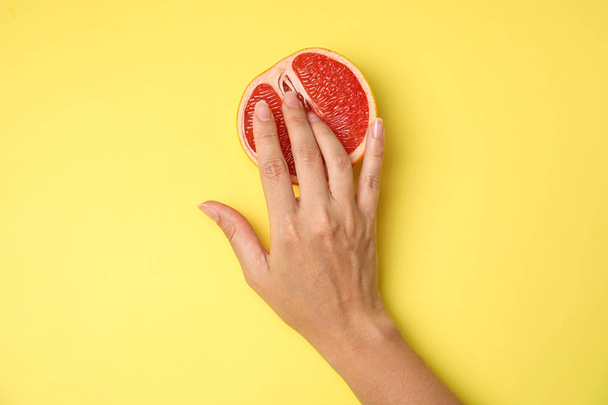 Young woman touching half of grapefruit on yellow background, top view. Sex concept - Photo, Image