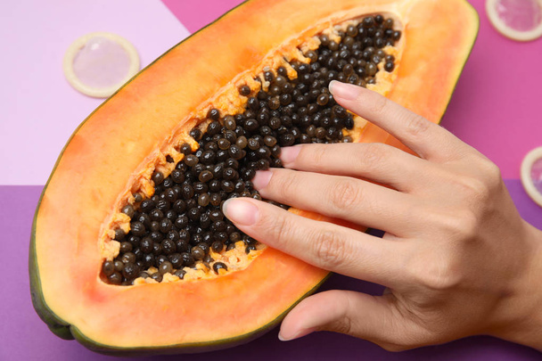 Young woman touching half of papaya and condoms on color background, closeup. Sex concept - Φωτογραφία, εικόνα