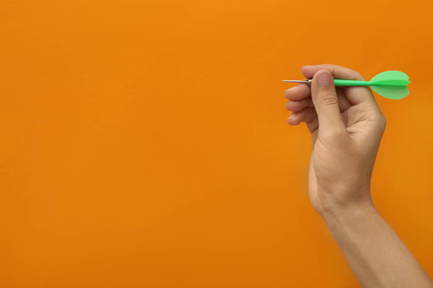 Woman holding green dart on orange background, closeup. Space for text - Foto, Imagem