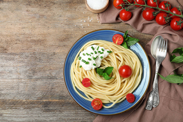 Delicious spaghetti with sour cream served on wooden table, flat lay. Space for text - Zdjęcie, obraz
