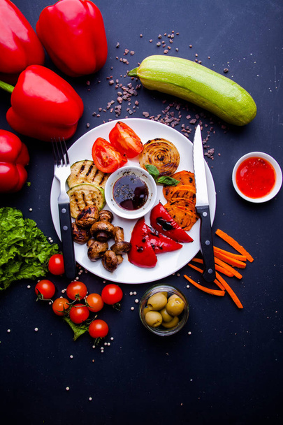 Veggy Suculentas verduras a la parrilla con una variedad de pimientos dulces, médula de bebé y tomate adornado con hierbas servidas en un plato con ingredientes visibles detrás
 - Foto, imagen