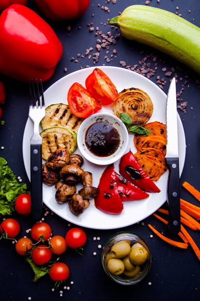 Veggy Παχύρευστα ψητά λαχανικά με ανάμικτες πιπεριές, μυελό των μωρών και ντομάτα γαρνιρισμένη με μυρωδικά σερβιρισμένα σε πιάτο με υλικά ορατά από πίσω - Φωτογραφία, εικόνα