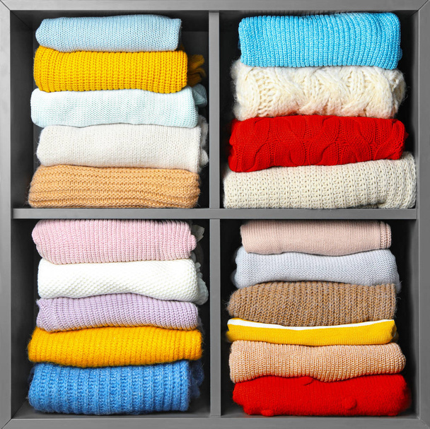 Many knitted winter clothes stacked on shelves near white background - Valokuva, kuva