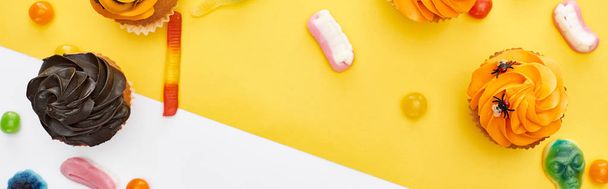 panoramic shot of colorful gummy sweets and cupcakes on yellow and white background, Halloween treat - Zdjęcie, obraz