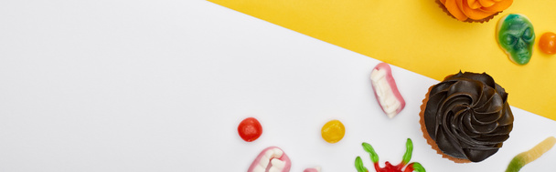 Panoramaaufnahme bunter Gummibärchen und Cupcakes auf gelb-weißem Hintergrund, Halloween-Leckereien - Foto, Bild