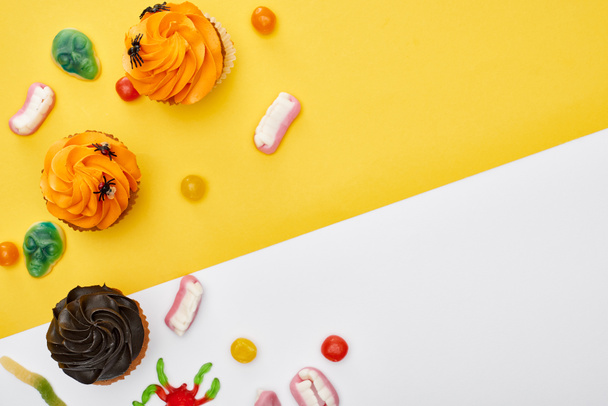 sarı ve beyaz arka plan üzerinde renkli sakızlı tatlılar ve cupcakes üst görünümü, Halloween tedavi - Fotoğraf, Görsel