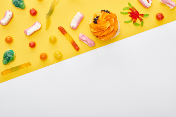 top view of colorful gummy sweets and cupcake on yellow background and white with copy space, Halloween treat - Photo, Image