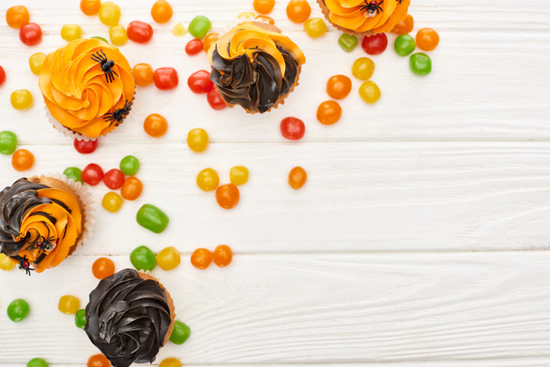 vista superior de bombons coloridos e cupcakes na mesa de madeira branca, deleite de Halloween
 - Foto, Imagem