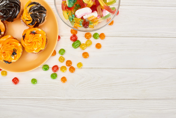 top view of colorful gummy sweets, bonbons and cupcakes on white wooden table, Halloween treat - Photo, Image