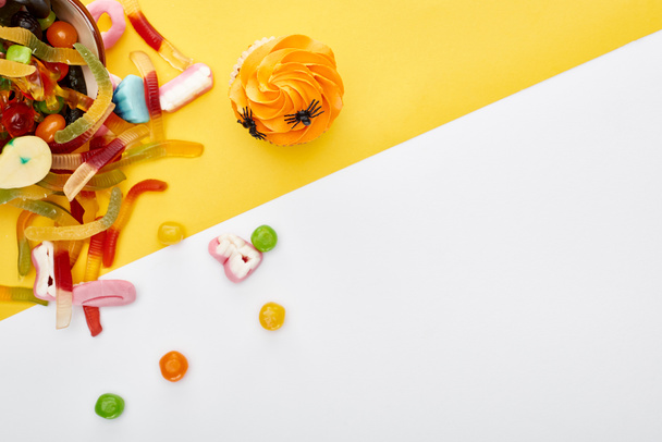 top view of colorful gummy worms near cupcake on white and yellow background, Halloween treat - Foto, afbeelding