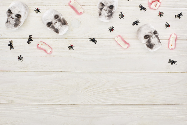 von oben: Gummizähne, Totenköpfe und Spinnen auf weißem Holztisch, Halloween-Leckerbissen - Foto, Bild