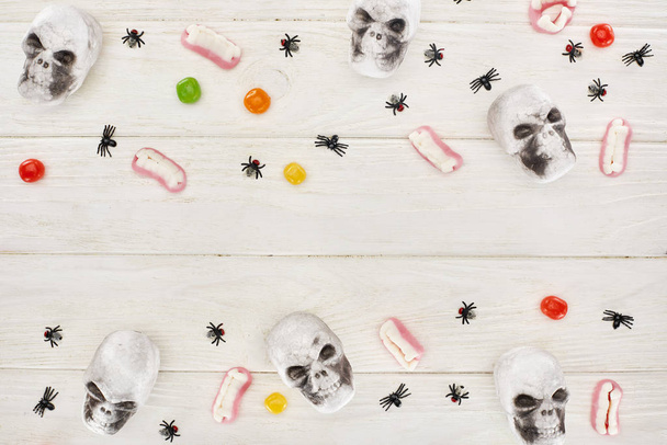 Top uitzicht van bonbons, Gummy tanden, schedels en spinnen op witte houten tafel, Halloween traktatie - Foto, afbeelding
