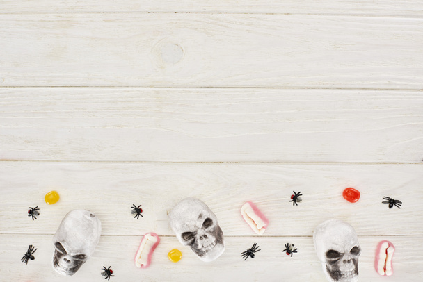 top view of bonbons, gummy teeth, skulls and spiders on white wooden table with copy space, Halloween treat - Photo, Image