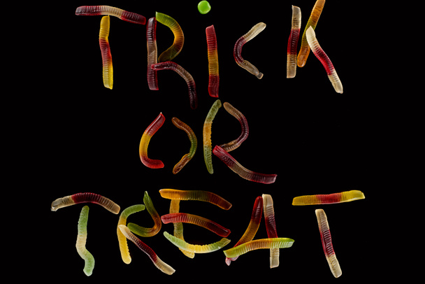 ylhäältä näkymä värikäs temppu tai hoitoon kirjaimet valmistettu gummy matoja eristetty musta, Halloween hoitoon
 - Valokuva, kuva