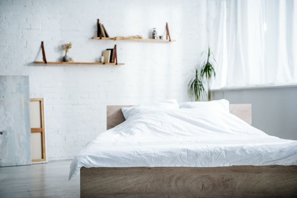 Schlafraum mit Bett, Kissen, Decke, Regalen und Pflanzen  - Foto, Bild